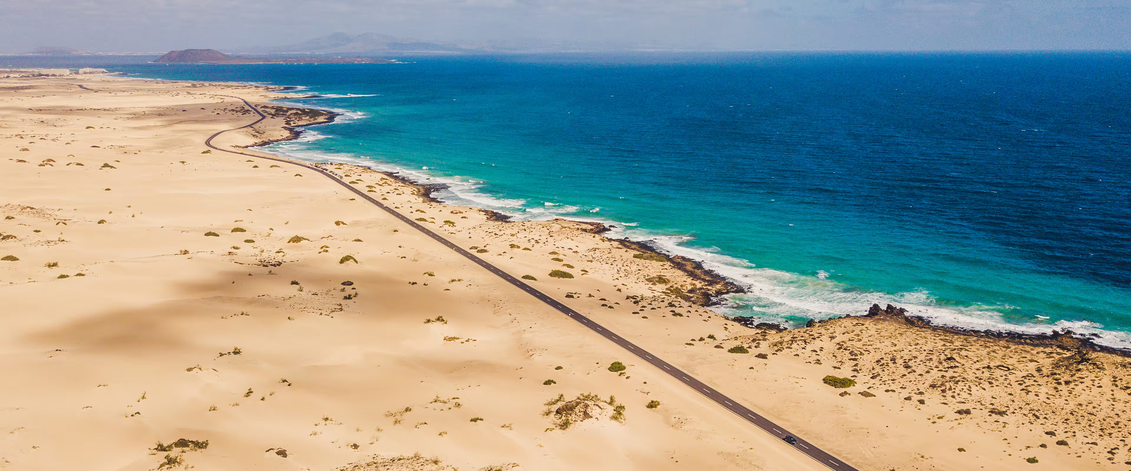 Vista aérea una carretera llena de dunas junto a la costa en Fuerteventura